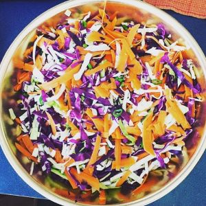 Food prepping an oriental chicken salad made with red and green cabbage, carrots, green onions, pineapple, chicken and homemade Apple Cider Vinegar dressing.